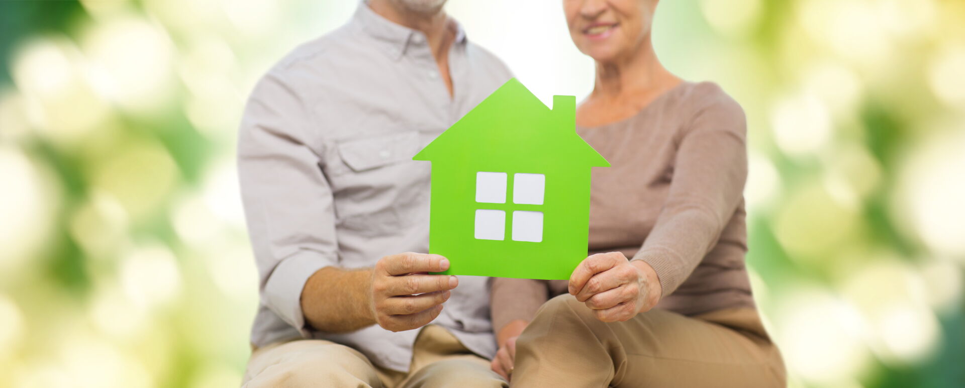 Paar hält grünes Papiermodell eines Hauses. Schnitzler Immobilien Lahr: Ihr glückliches Zuhause.